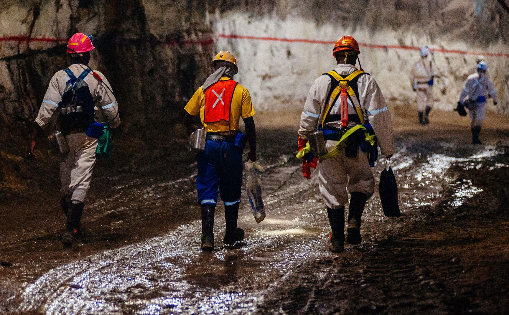 Mineworkers walking in a mine tunnel, wearing helmets and safety gear